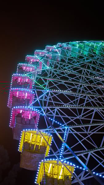 Detalle de una noria iluminada por la noche, con cabinas de colores y estructura metálica resaltada por luces LED. La imagen transmite diversión, ocio y ambiente festivo, asociada a ferias o eventos navideños en ciudades.