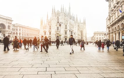 Personas caminando por la Plaza del Duomo de Milán frente a la catedral gótica, con ambiente urbano y movimiento cotidiano.