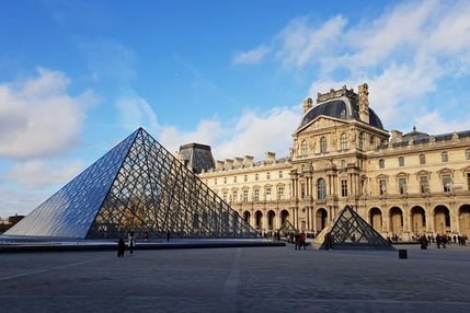 Pirámide de cristal del Museo del Louvre en París, junto al histórico palacio, bajo un cielo despejado