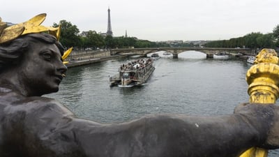 Barco turístico navegando por el río Sena en París con la Torre Eiffel al fondo y esculturas del puente en primer plano