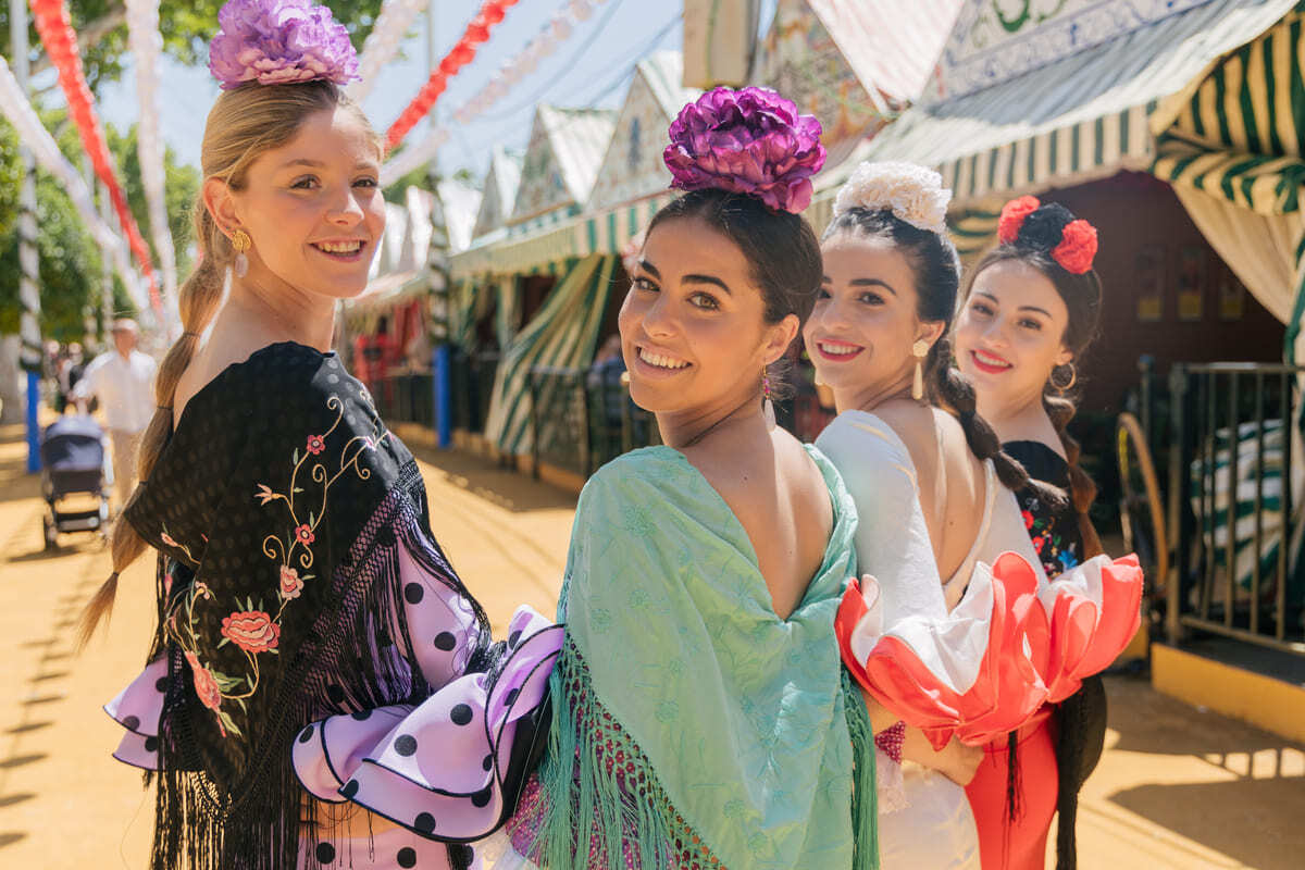 Cuatro mujeres vestidas de flamenca sonrién posando en una calle de la Feria de Abril de Sevilla