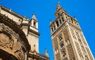 Vista desde abajo de la Giralda de Sevilla, antiguo alminar almohade convertido en campanario de la Catedral, con cielo azul despejado.