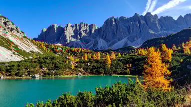 Paisaje del lago di Anterselva rodeado de bosques y montañas alpinas, con agua turquesa y colores otoñales.