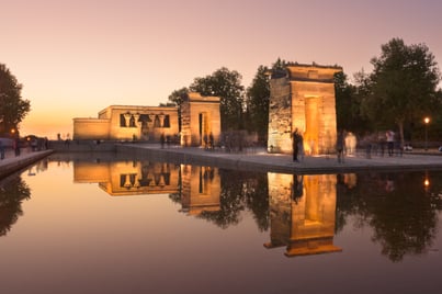 Templo de Debod en Madrid al atardecer, reflejado en el estanque, con visitantes alrededor en movimiento.