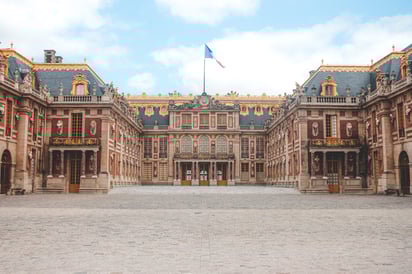 Fachada principal del Palacio de Versalles en París con jardines y visitantes frente al edificio