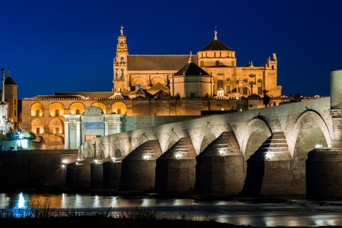 Mezquita-Catedral de Córdoba iluminada de noche junto al Puente Romano sobre el río Guadalquivir.