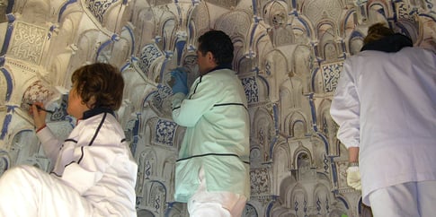 Restauradores trabajando en las yeserías nazaríes de la Alhambra, consolidando detalles decorativos con técnicas manuales.