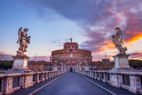 Castel Sant’Angelo al atardecer visto desde el puente, con estatuas y cielo de colores.