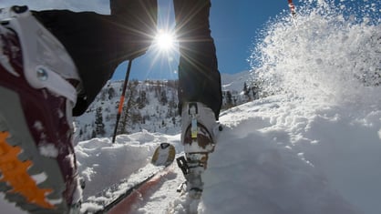 Detalle de una persona practicando esquí de montaña, avanzando por la nieve con esquís y bastones bajo el sol.
