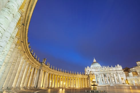 Plaza y columnata de San Pedro iluminadas de noche, con la basílica al fondo.