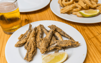 Plato de pescado frito con una cuña de limón y una cerveza en una mesa de bar.