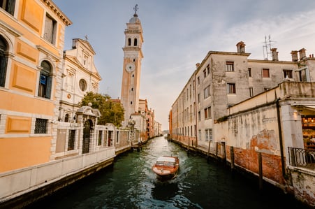 Embarcación tradicional navegando por un canal de Venecia, con edificios históricos y una iglesia junto al agua.