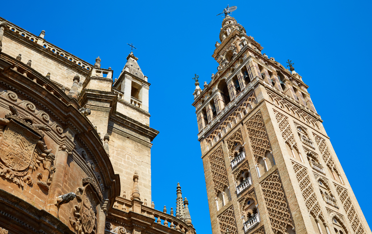 Vista desde abajo de la Giralda de Sevilla, antiguo alminar almohade convertido en campanario de la Catedral, con cielo azul despejado.